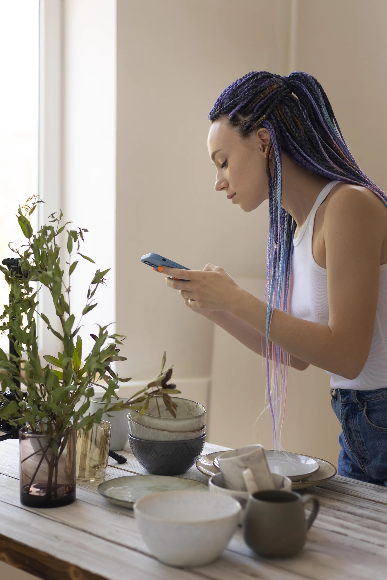 Mulher fotografando louças com o celular em uma mesa de trabalho